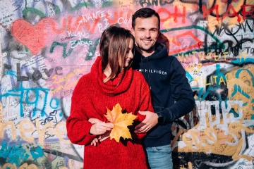 Pár pózující před graffiti zdí, žena v červeném svetru drží javorový list.