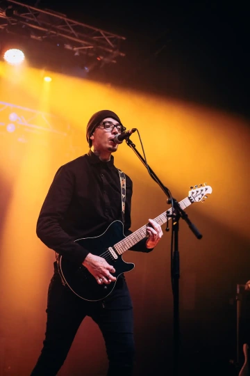 Hudebník s kytarou zpívá do mikrofonu na osvětleném pódiu.