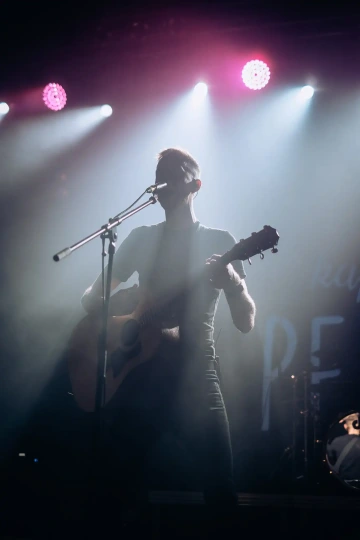 Muzikant hraje na akustickou kytaru pod pódiovými světly.