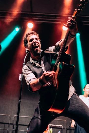 Muzikant nadšeně hrající na kytaru na jevišti, osvětlen barevnými reflektory.