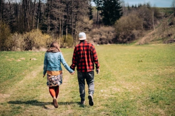 Pár kráčející ruku v ruce po louce směrem k lesu.