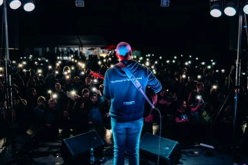 Hudebník na pódiu před davem s rozsvícenými telefony.