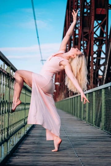 Tanečnice v růžových šatech provádí baletní pózu na mostě.