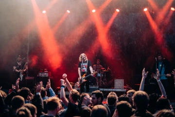 Kapela vystupující na pódiu se světelnými efekty a nadšeným publikem.