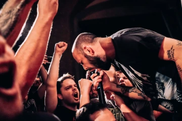 Zpěvák křičící do mikrofonu uprostřed nadšeného davu na koncertě.